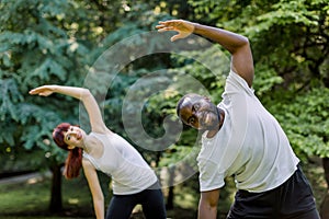 Active healthy couple, African guy and Caucasian girl, working out together outdoors, doing stretching exercises on the