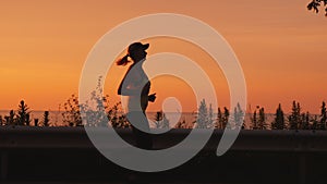 Active and healthy lifestyle - woman silhouette running along the road along the sea at sunset