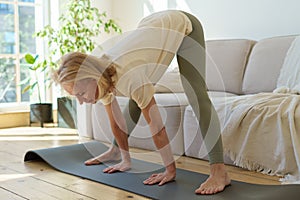 Active healthy senior woman standing in downward facing dog yoga pose while practicing yoga at home