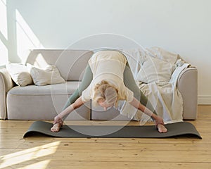 Active healthy senior woman standing in downward facing dog yoga pose while practicing yoga at home