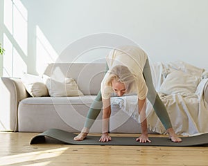 Active healthy senior woman standing in downward facing dog yoga pose while practicing yoga at home