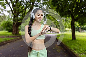 Active indian woman checking fitness tracker during park workout in green tracksuit