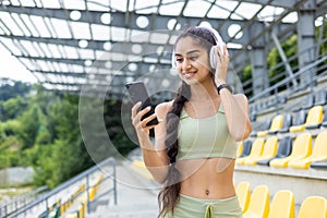 Active indian woman using smartwatch and smartphone while jogging in stadium outdoors