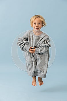 Active jumping toddler boy in a huge oversized grey longsleeve over blue