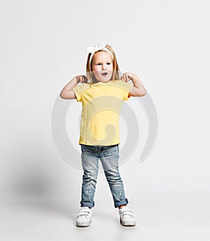 Active kid baby girl in yellow t-shirt is singing nursery rhyme dancing doing exercises with her hands on her shoulders