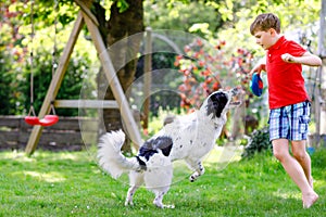 Active kid boy playing with family dog in garden. Laughing school child having fun with dog, with running and playing