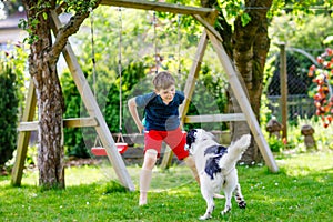 Active kid boy playing with family dog in garden. Laughing school child having fun with dog, with running and playing