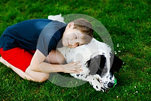 Active kid boy playing with family dog in garden. Laughing school child having fun with dog, with running and playing