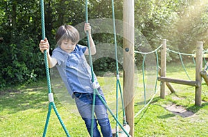 Active kid climbing rope in the playground,, Child enjoying activity in a climbing adventure park on summer sunny day, Cute little