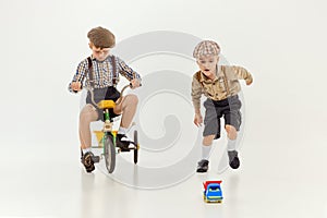 Active kids. Boys, childred in retro clothes riding vintage bicycle over grey studio background. Concept of game