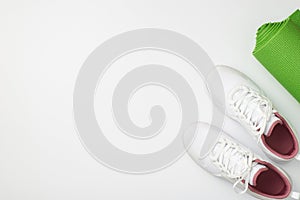 Active lifestyle concept. Top view photo of white sneakers and green sports mat on isolated white background with copyspace