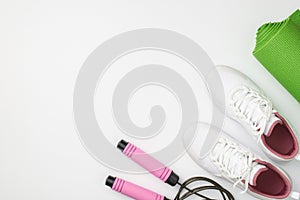 Active lifestyle concept. Top view photo of white sneakers green sports mat and skipping rope on isolated white background with