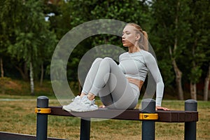 Active lifestyle. Slim blond woman working out in outdoor gym at summer warm day.