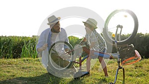 Active lifestyle, Ñurious child and father repairing bicycle at rural on background of nature in backlight