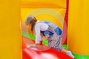 An active Little girl is playing on a colored inflatable slide. A small child is having fun on an inflatable trampoline. A happy,