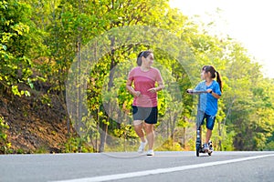 Active little girl riding a scooter on a park road on a summer day with her mother. Outdoor sports for children. Family spending