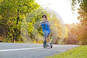 Active little girl riding a scooter on the road in the park on a summer day. Cute little girl wearing helmet enjoys riding kick