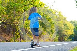 Active little girl riding a scooter on the road in the park on a summer day. Cute little girl wearing helmet enjoys riding kick