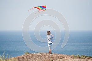 Active little kid holding flying color kite in air above blue ocean and sky in summer leisure games