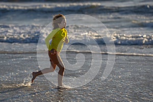 Active little kid running along sea beach during leisure sport activity. Sporty kid running in nature. Child run at