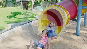 Active little sisters playing on colorful slide in the outdoor playground. Happy child girls smiling and laughing on children play