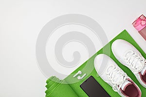 Active living concept. Top view photo of pink bottle white sneakers smartphone and earbuds over green exercise mat on isolated