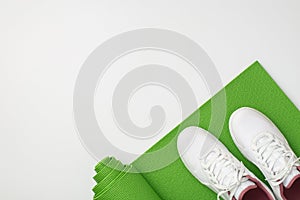Active living concept. Top view photo of white sneakers over green exercise mat on isolated white background with copyspace