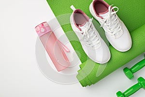 Active living concept. Top view photo of white sneakers pink bottle of water green sports mat and dumbbells on isolated white