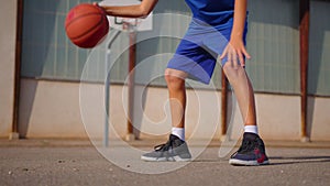 Active male basketball player practicing ball handling skill, dribbling ball between legs on outdoor court in rays of