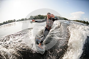 Active male surfer riding foaming river wave from motorboat