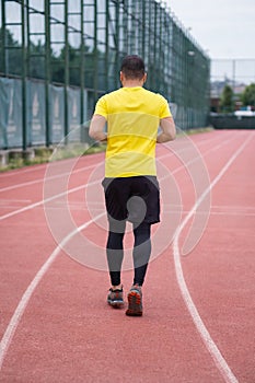 Active man in activewear jogs along the stadium track, healthy and active lifestyle backside view