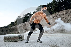 Active man with bare torso pulling tyre on long chain