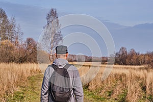 Active man in casual with backpack is walking in a meadow late autumn. Siberia, Russia