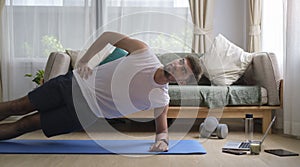 Active man doing side plank exercise on mat in bright living room. Sport, fitness and healthy lifestyle concept