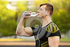 Active man drinking water from a bottle, outdoor. Muscular male quenches thirst photo