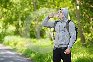 Active man drinking water from a bottle, outdoor. Young muscular male quenches thirst photo