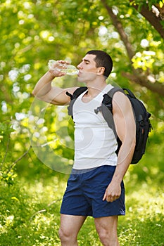 Active man drinking water from a bottle, outdoor. Young muscular male quenches thirst