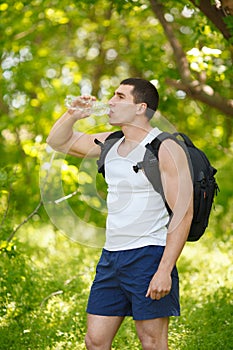 Active man drinking water from a bottle, outdoor. Young muscular male quenches thirst