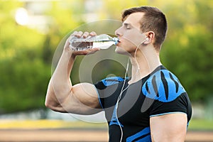 Active man drinking water from a bottle, outdoors. Young fit male quenches thirst