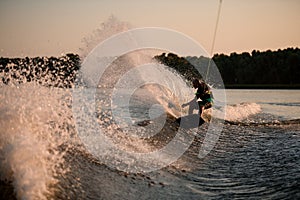 active man energetically balancing on great splasing wave on wakesboard.