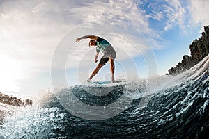active man energetically balancing on wave on wakesurf board on splashing wave.