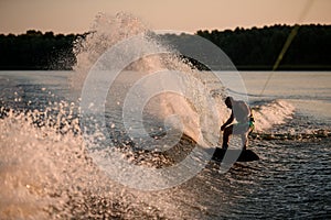 active man energetically rides down on splasing wave on wakesboard.