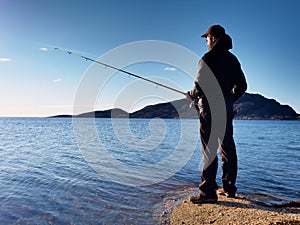 The active man is fishing on sea from the rocky coast. Fisherman check pushing bait