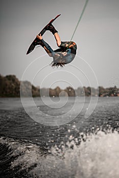 active man doing extreme high jump on wakeboard over splashing river wave