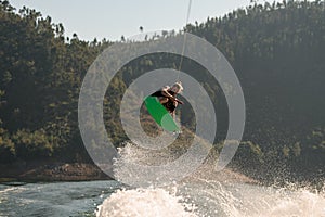 active man holds rope and jumping with wakeboard over splashing water.