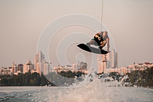 active man holds rope and skilfully jumping high in air on wakeboard over splashing water.
