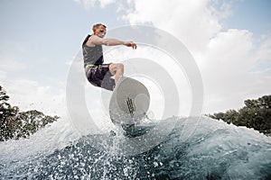 Active man jumping up on the white wakeboard on the high wave