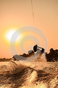 active man making trick with wakeboard on bright orange sky and sun background.