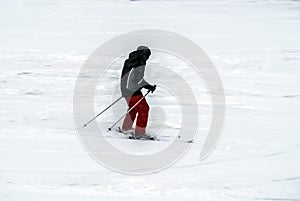 Active man ski riding on slope. Male skier moving on white snow. Side view of male in gray coat and red pants rides downhill.