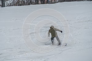 Active man snowboarder riding on slope. Man snowboarder snowboarding on white snow. Back view of male in khaki green coat and gray